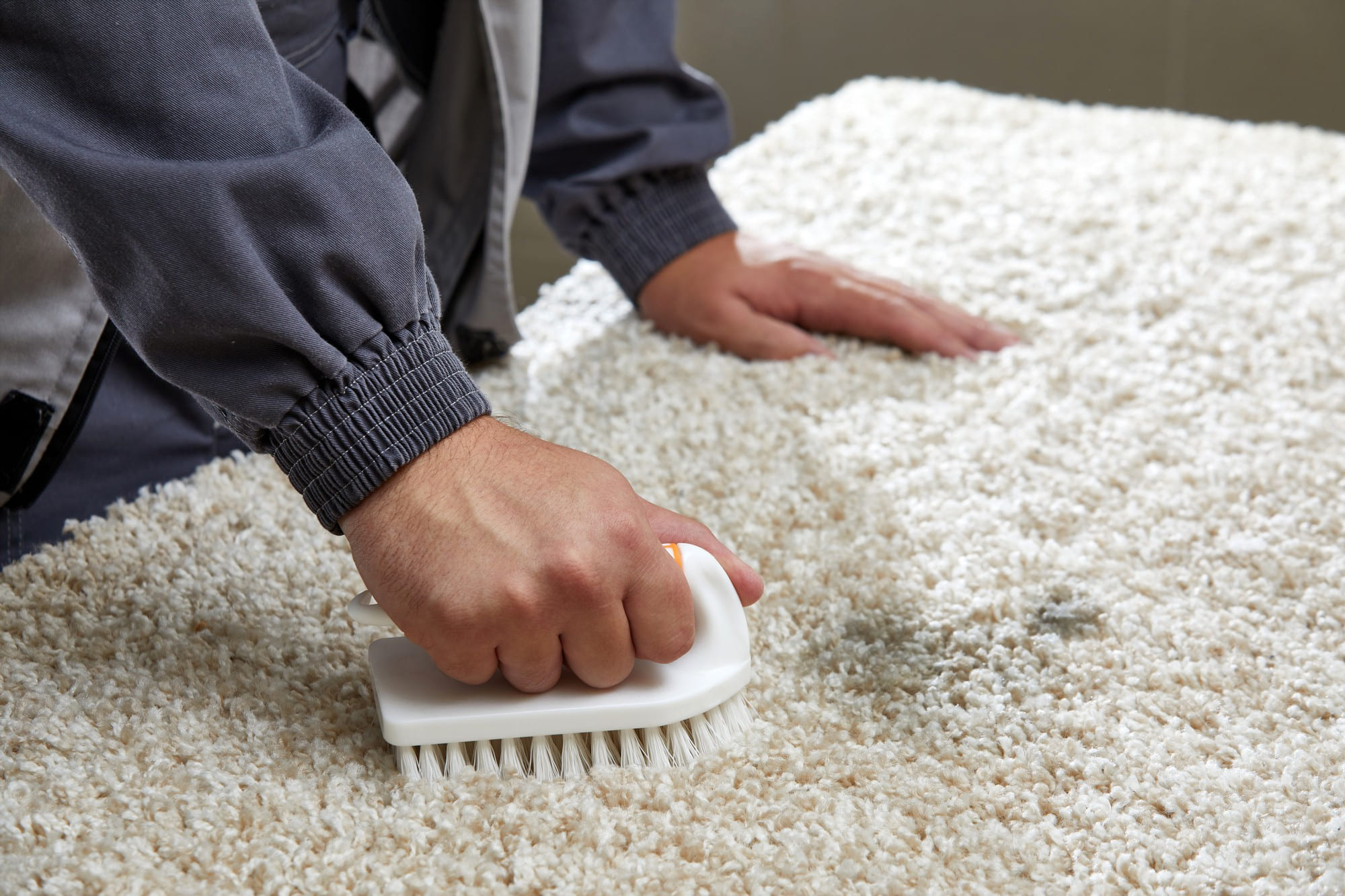 A man uses a brush to clean dirt from a grey carpet